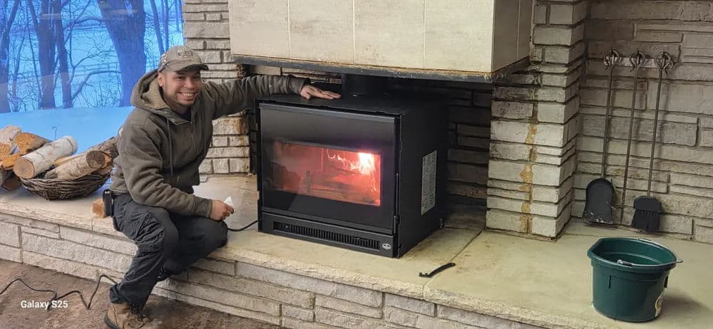 Man adjusting a modern fireplace in a cozy stone living area with firewood nearby.
