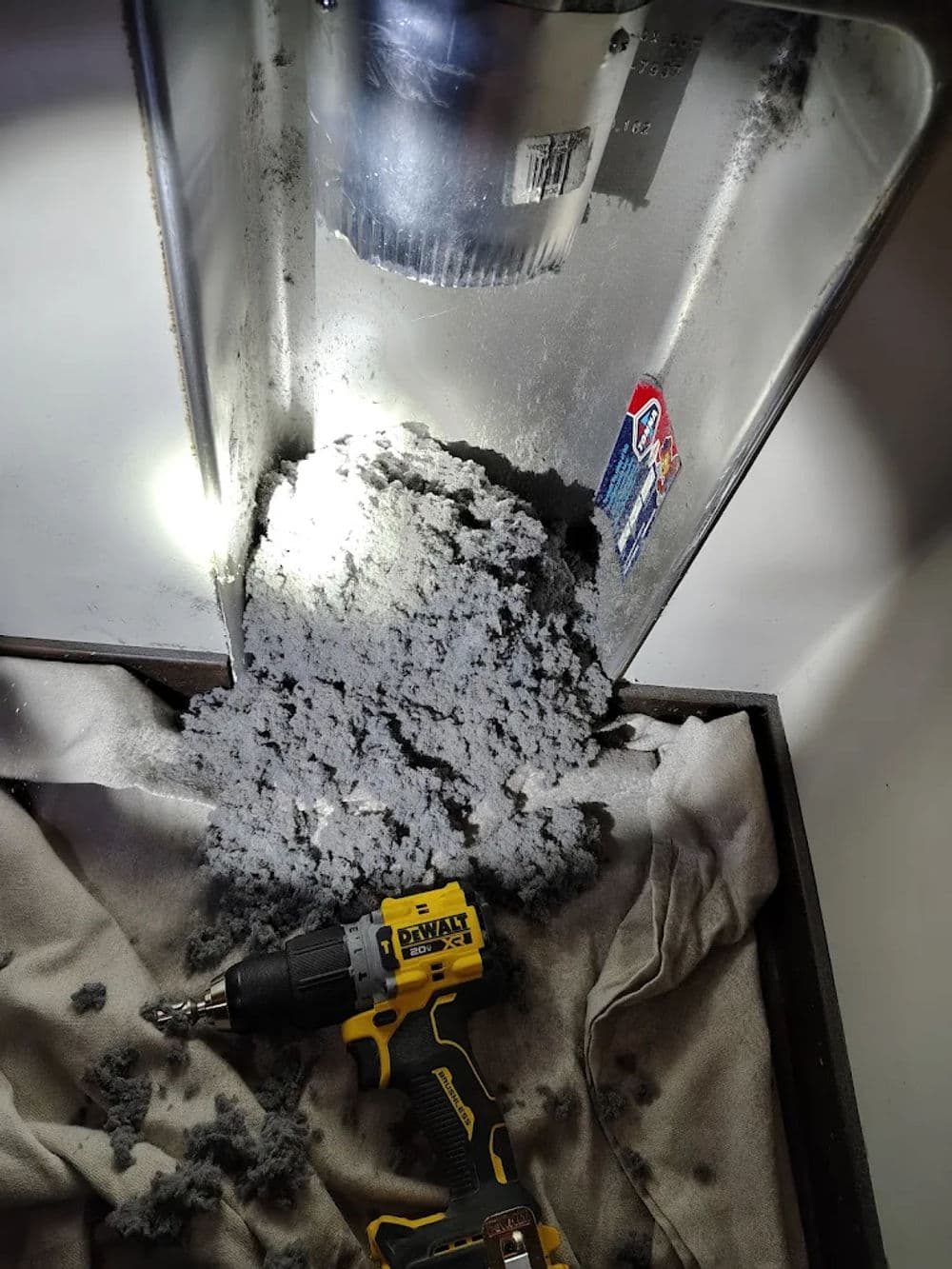 Drill next to dryer vent with lint buildup and tools, highlighting home maintenance need.