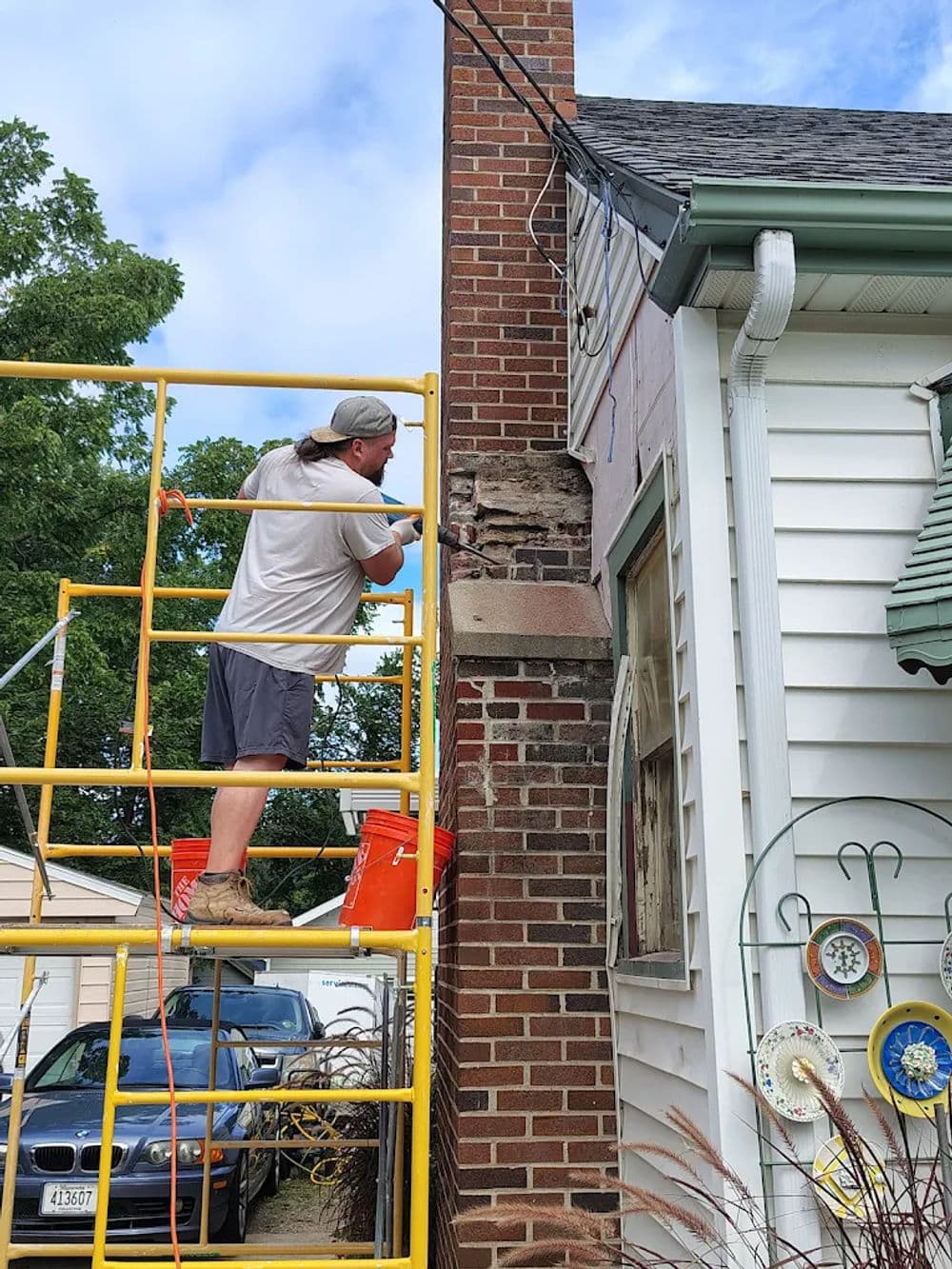 Contractor repairing chimney on residential home using scaffolding and tools.